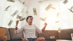 A man surrounded by falling money on a couch, symbolizing the best travel agency in Dubai.