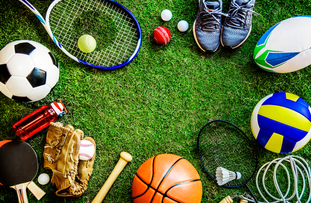 A variety of sports equipment—including balls and rackets—arranged neatly on a grassy field.jpg