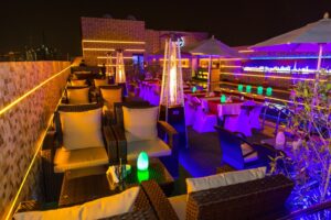 A rooftop bar illuminated with purple lighting, featuring stylish tables for guests to enjoy their drinks and views.jpg