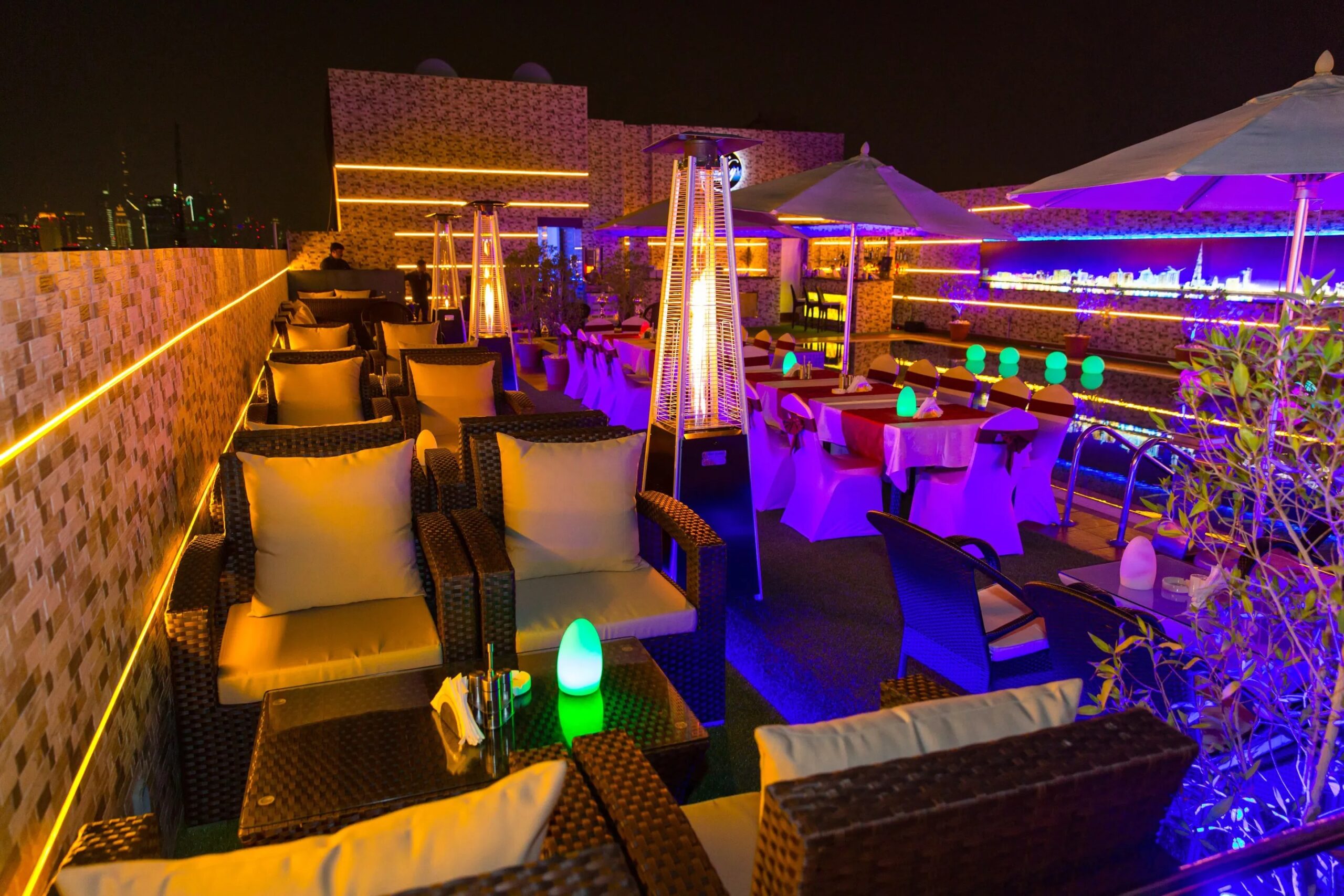 A rooftop bar illuminated with purple lighting, featuring stylish tables for guests to enjoy their drinks and views.jpg