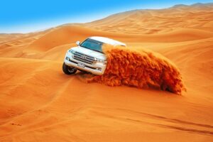 A white SUV traversing a vast desert landscape under a clear blue sky.jpg