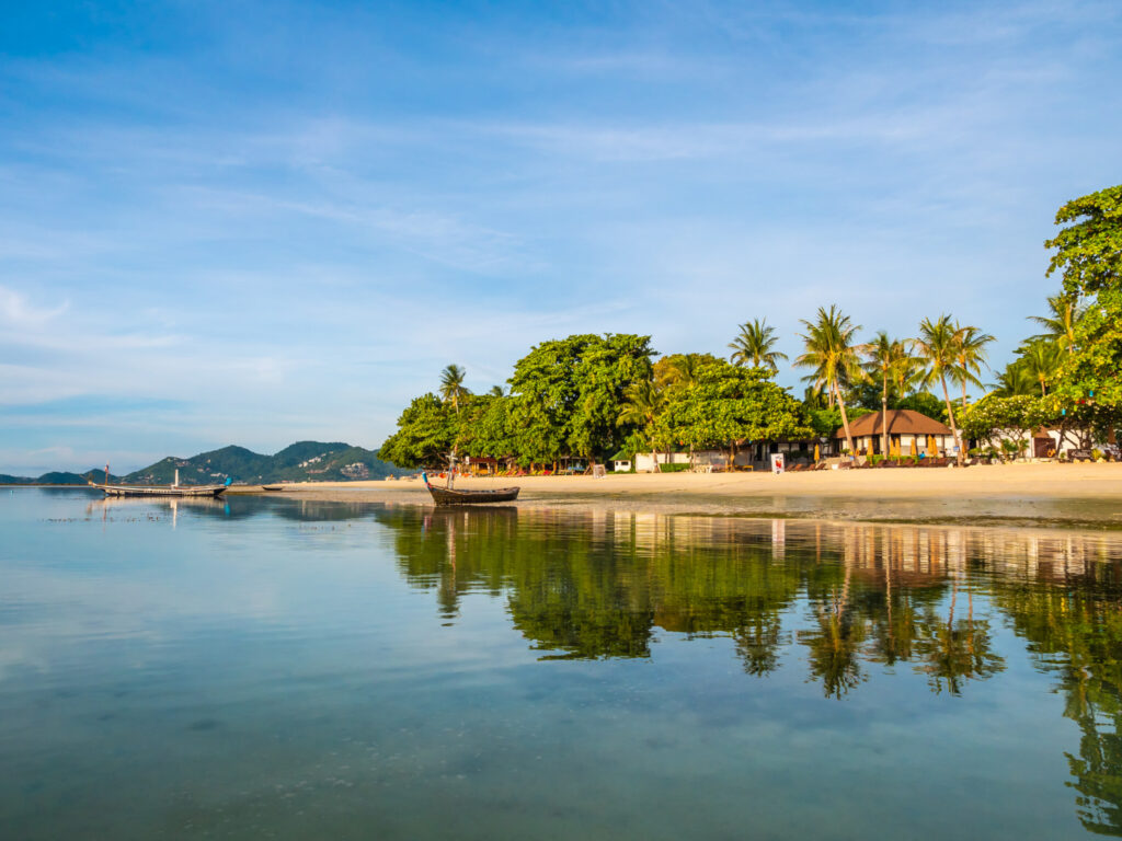 A-serene-beach-scene-featuring-a-boat-anchored-near-the-shore-surrounded-by-lush-trees-and-gentle-waves.jpg