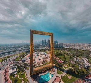 A large golden frame stands prominently in the center of a park, surrounded by lush greenery and open space.jpg