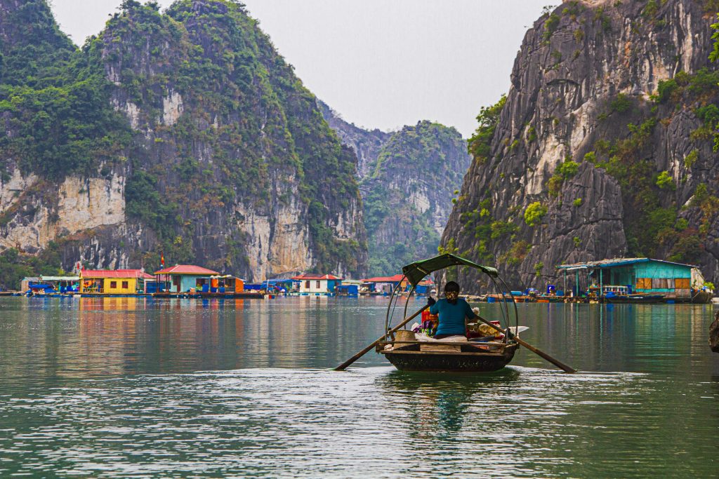 A man sits in a boat on tranquil water, surrounded by a stunning mountain landscape in the background.jpeg